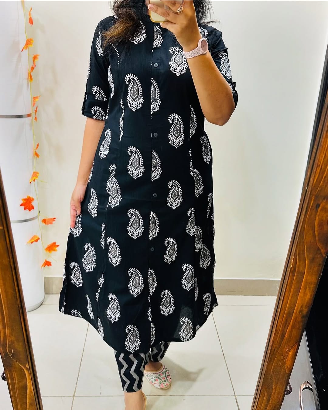Person wearing a black dress with white patterns in front of a mirror.