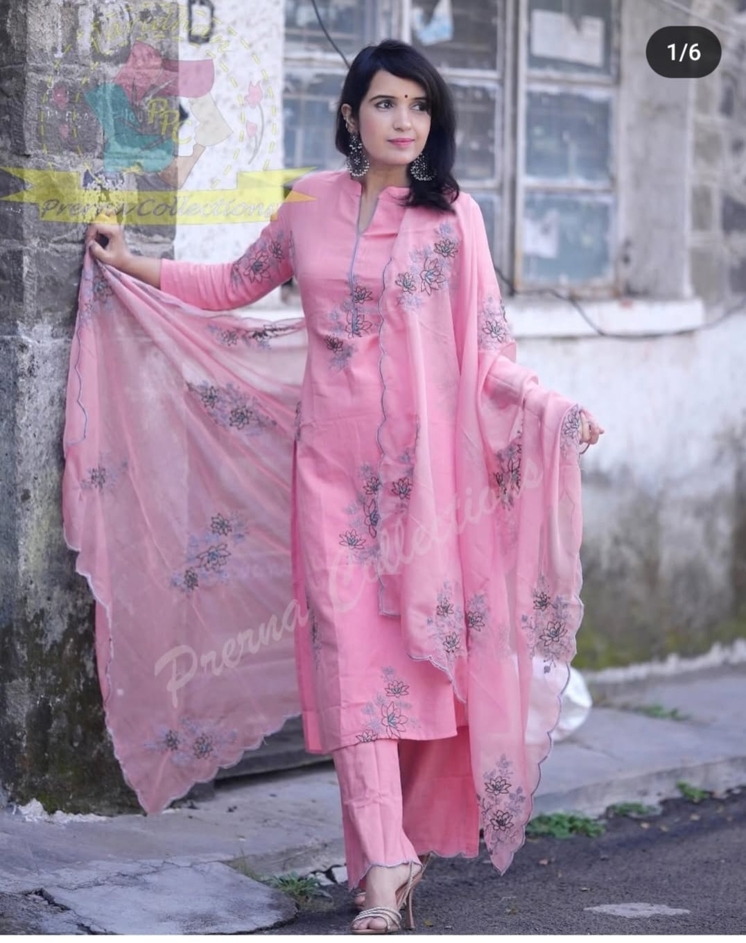 Woman in a pink traditional outfit with floral patterns standing against a wall.