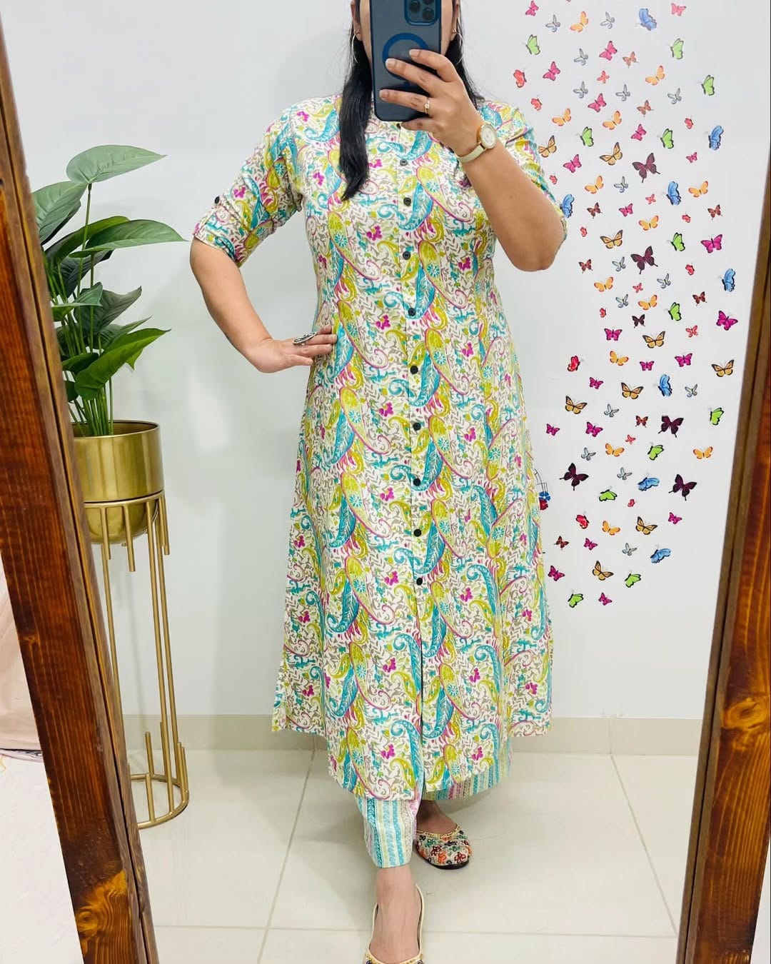 Person wearing a colorful floral dress in front of a mirror with a decorative wall in the background.