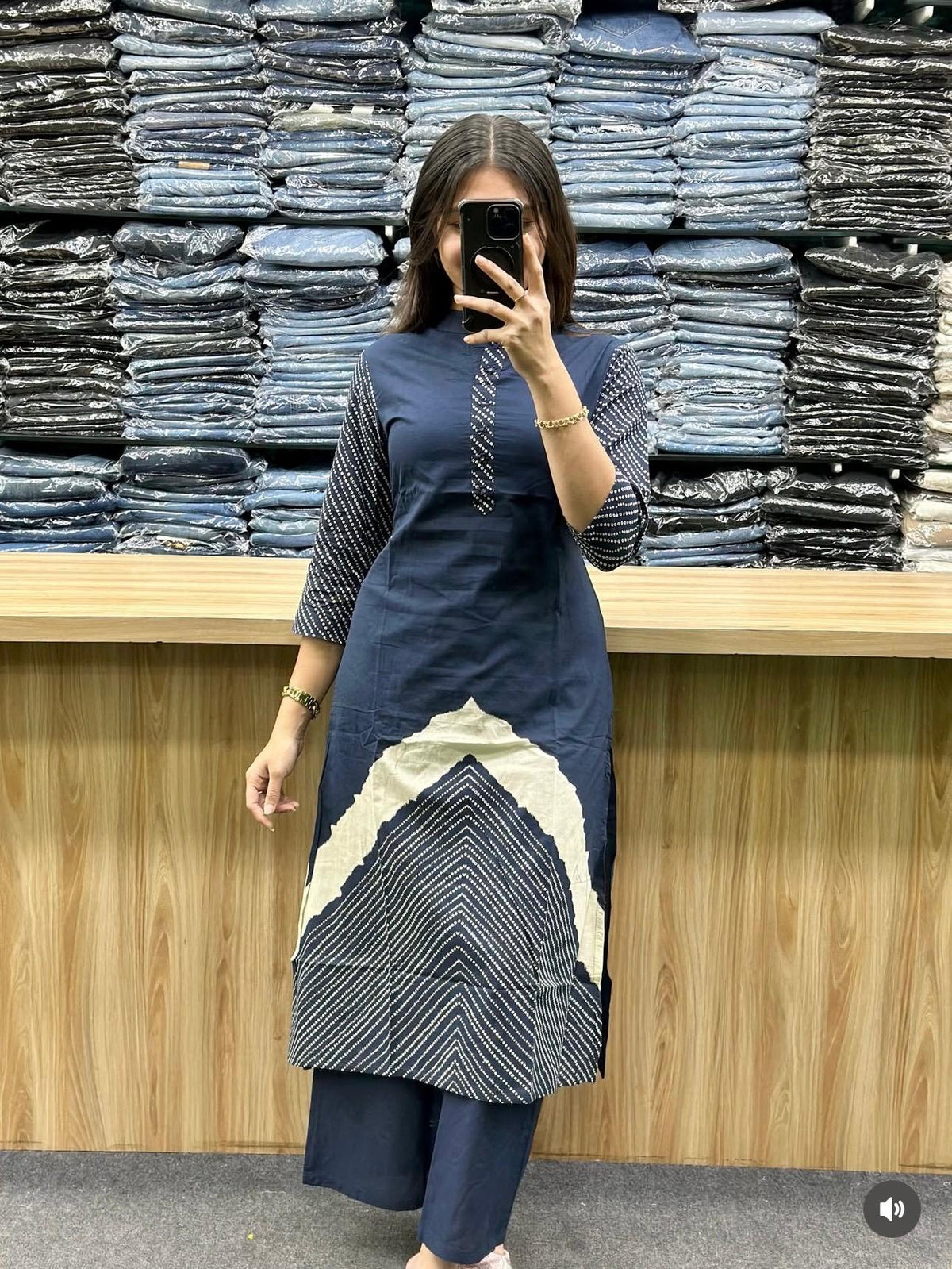 Person wearing a blue and white dress standing in front of stacks of jeans.
