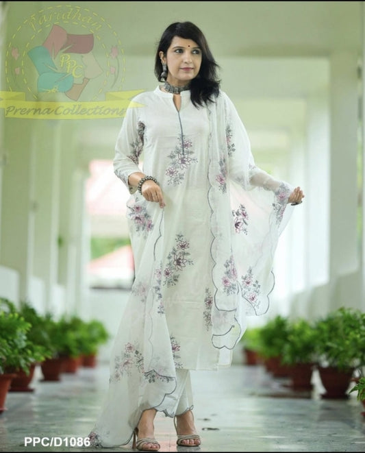 Woman in a white floral outfit standing in a corridor with plants.