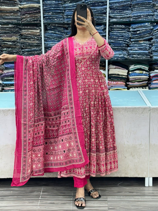 Person wearing a pink traditional outfit with a patterned dupatta in front of a stack of fabric.