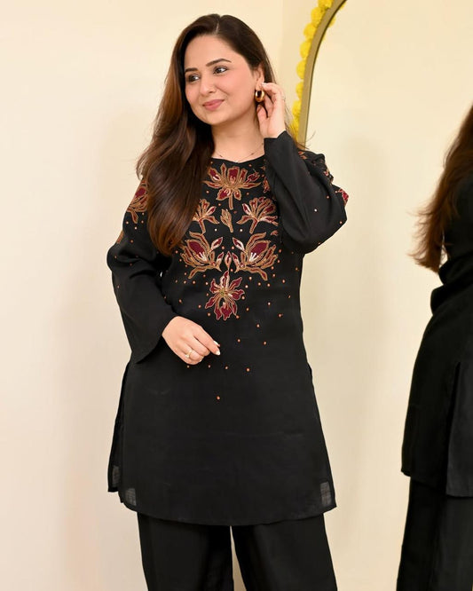 Woman wearing a black embroidered top and pants against a beige background