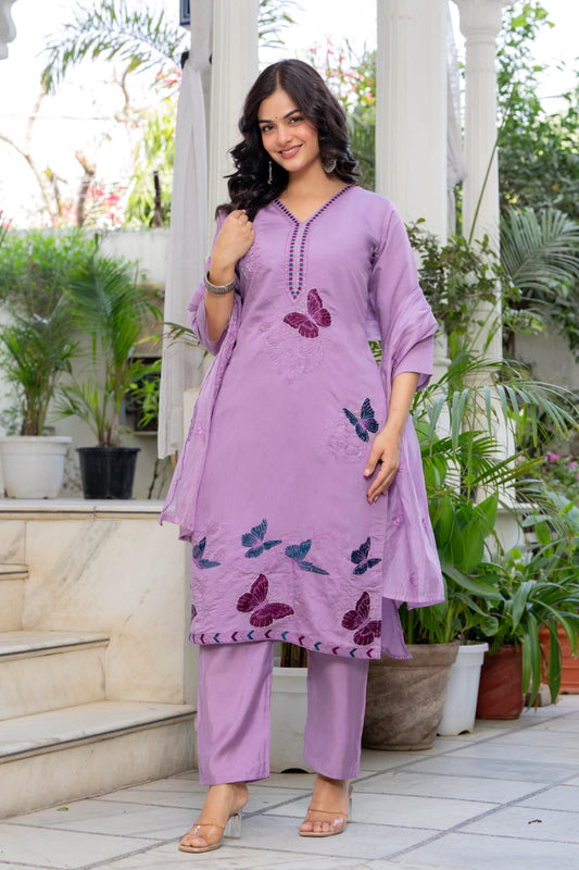Woman wearing a purple outfit with butterfly patterns in an outdoor setting.